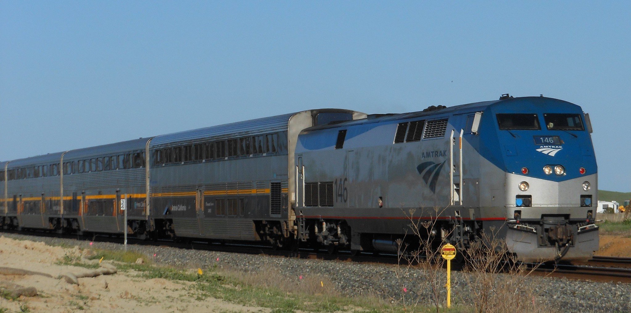 A silver and blue Amtrak train traveling on railway tracks with a clear sky in the background.