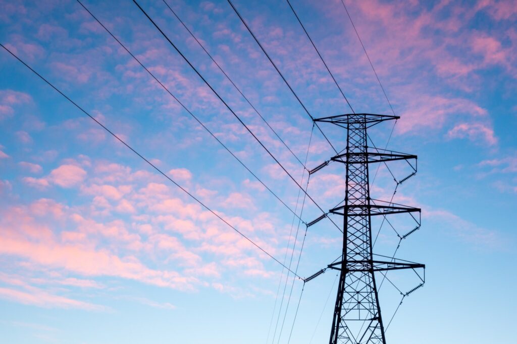 A high-voltage power tower against a colorful sky at sunset.