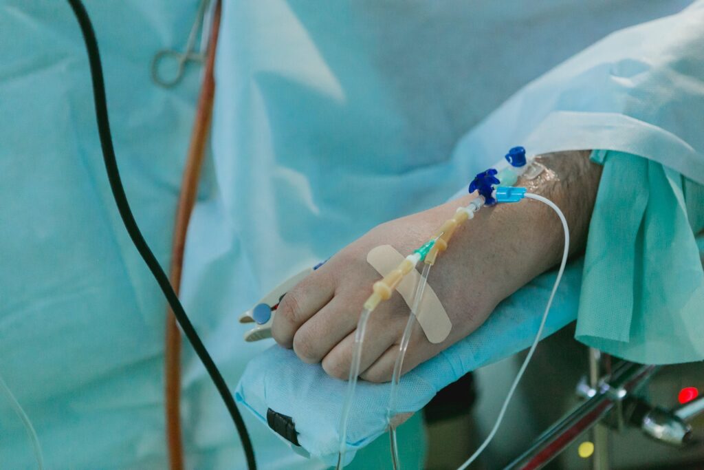A patient's hand with IV lines and monitors, covered in a surgical drape.
