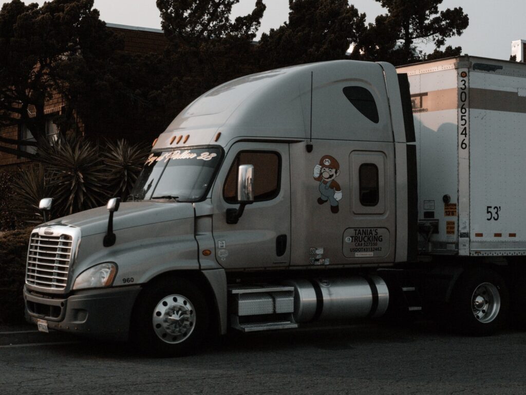 A silver semi-truck parked on the street with trees in the background.