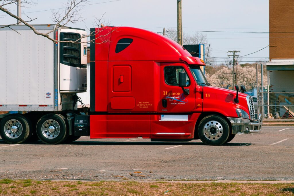 A red semi-truck parked in a lot, with a white trailer attached.