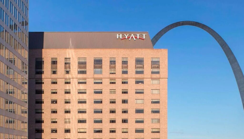 A Hyatt hotel building with an arch in the background under a clear blue sky.